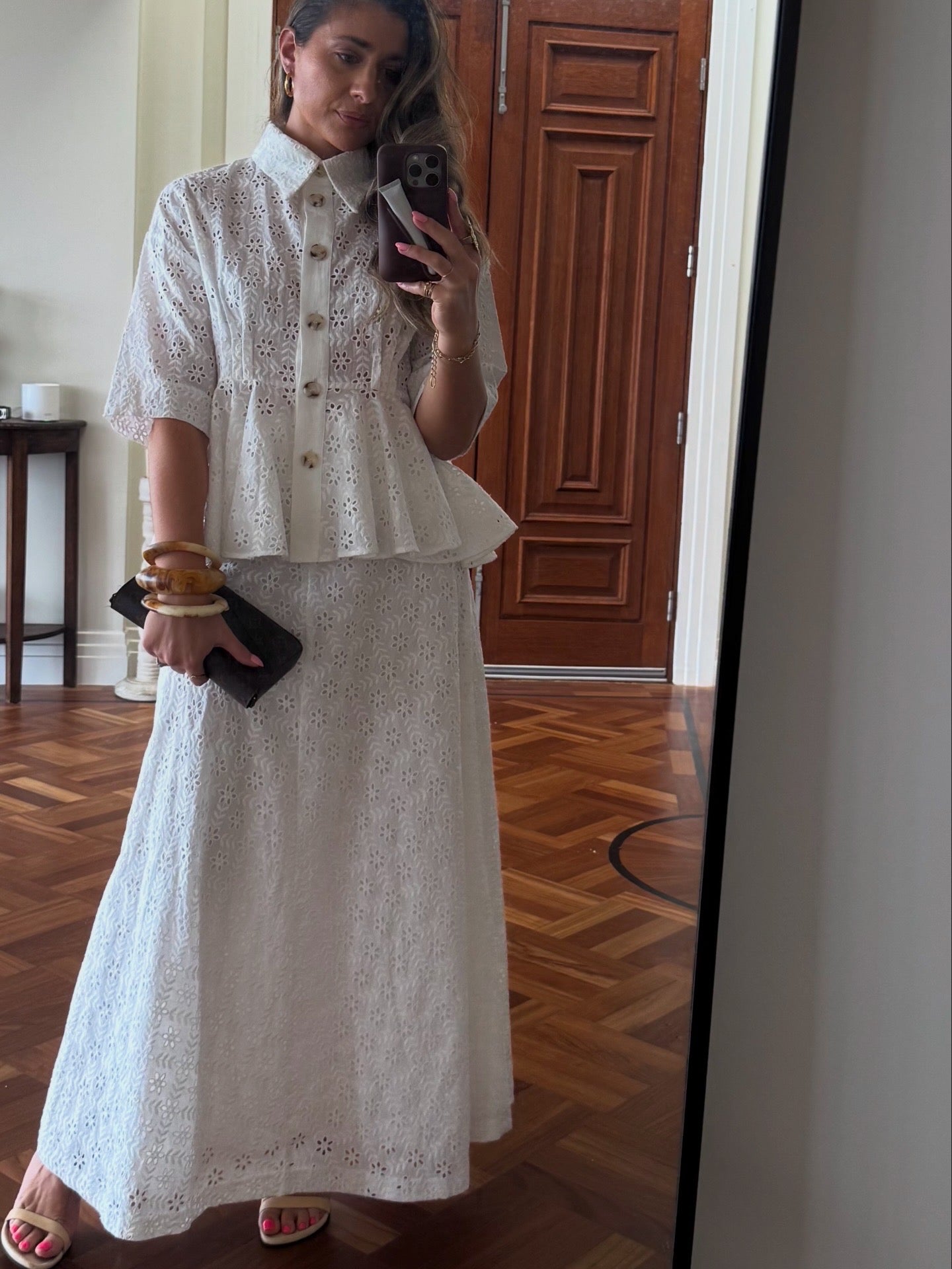 Woman taking a mirror selfie wearing a white lace outfit in a room with wooden flooring.