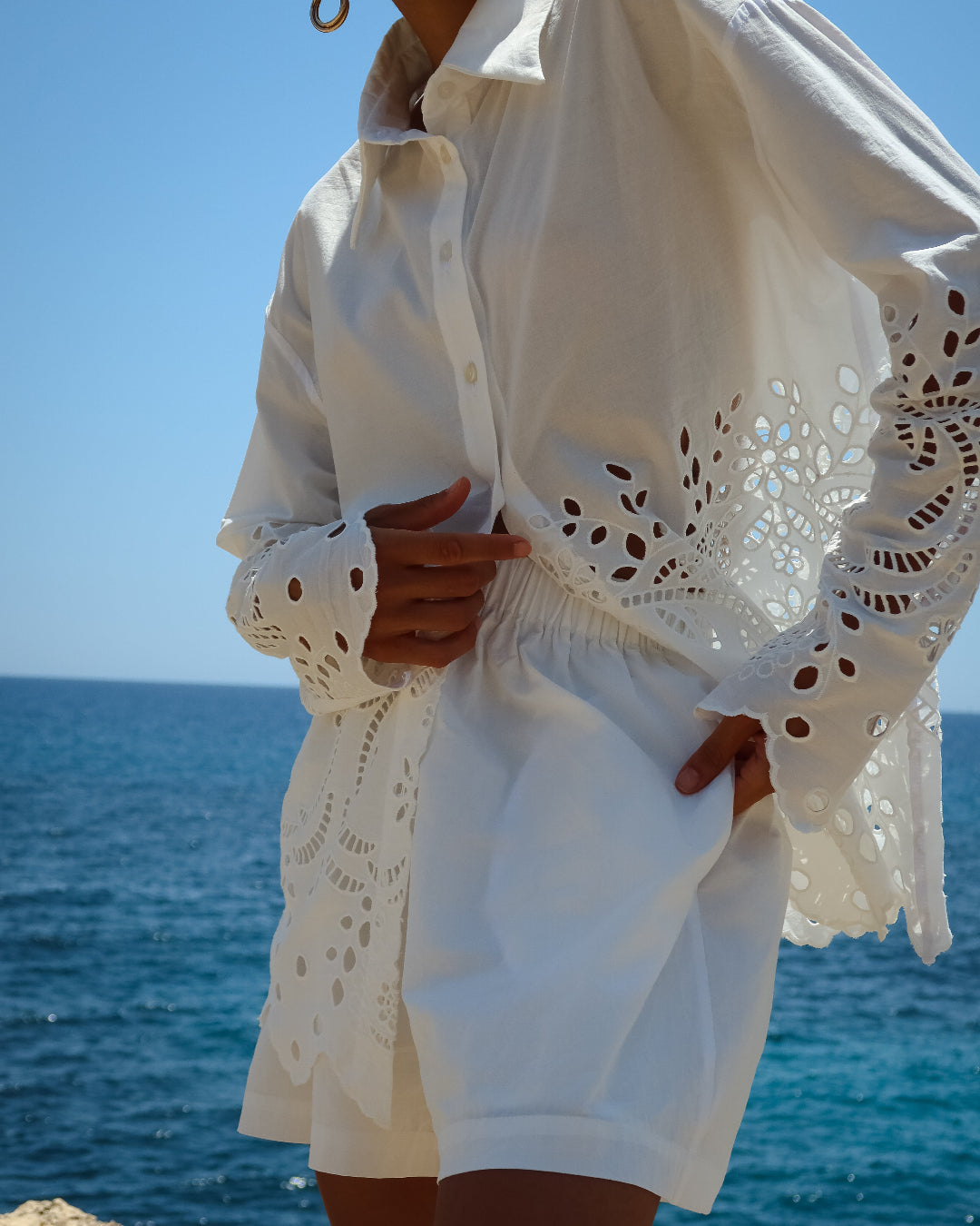 Person wearing a white outfit with lace details by the ocean