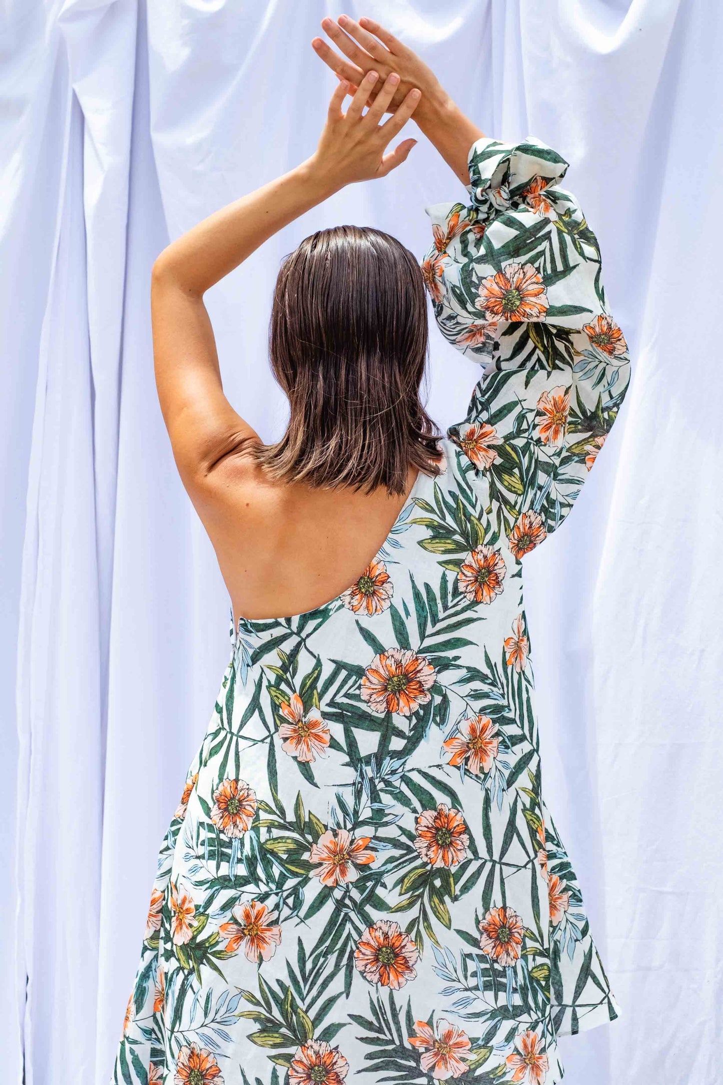 Woman facing away from camera, wearing Palm Balloon Sleeve Swing Dress by Isabella Longginou. She has both arms above her head.
